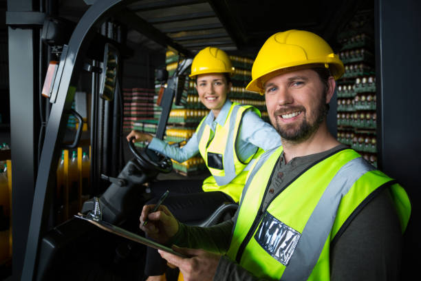 2 Personen blicken vor einem Gabelstapler in die Kamera